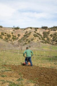 A farmer working with a tiller in an open countryside field, preparing the soil for planting.